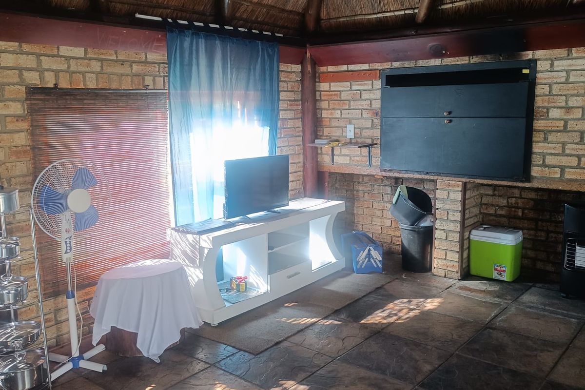Rustic entertainment area featuring a traditional thatched roof, exposed brick walls, and durable tiled flooring with a built-in braai unit.
