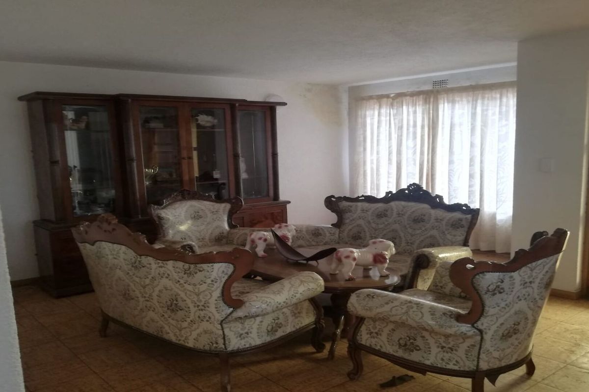 A living room featuring tiled flooring and a large window with curtains, showing signs of ceiling water damage.