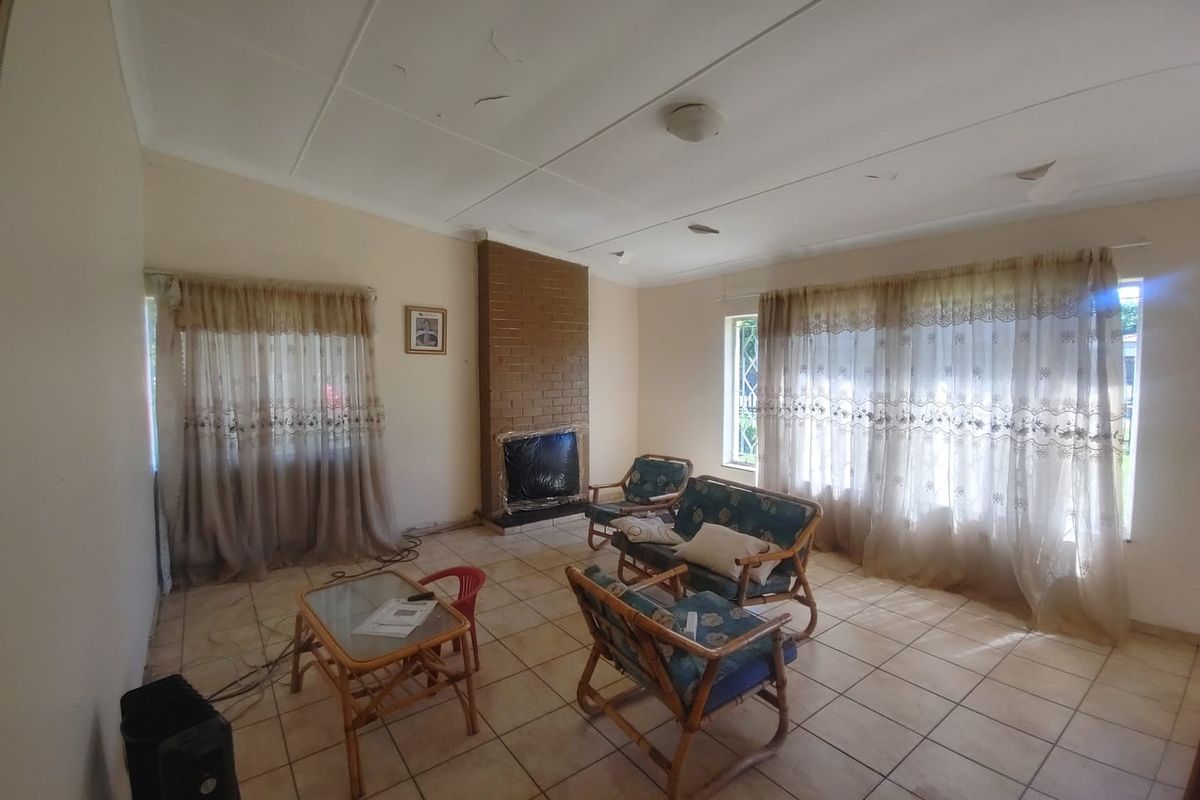 Spacious living room featuring a brick fireplace, tiled flooring, and large windows, offering a blank canvas for renovation and modernization.