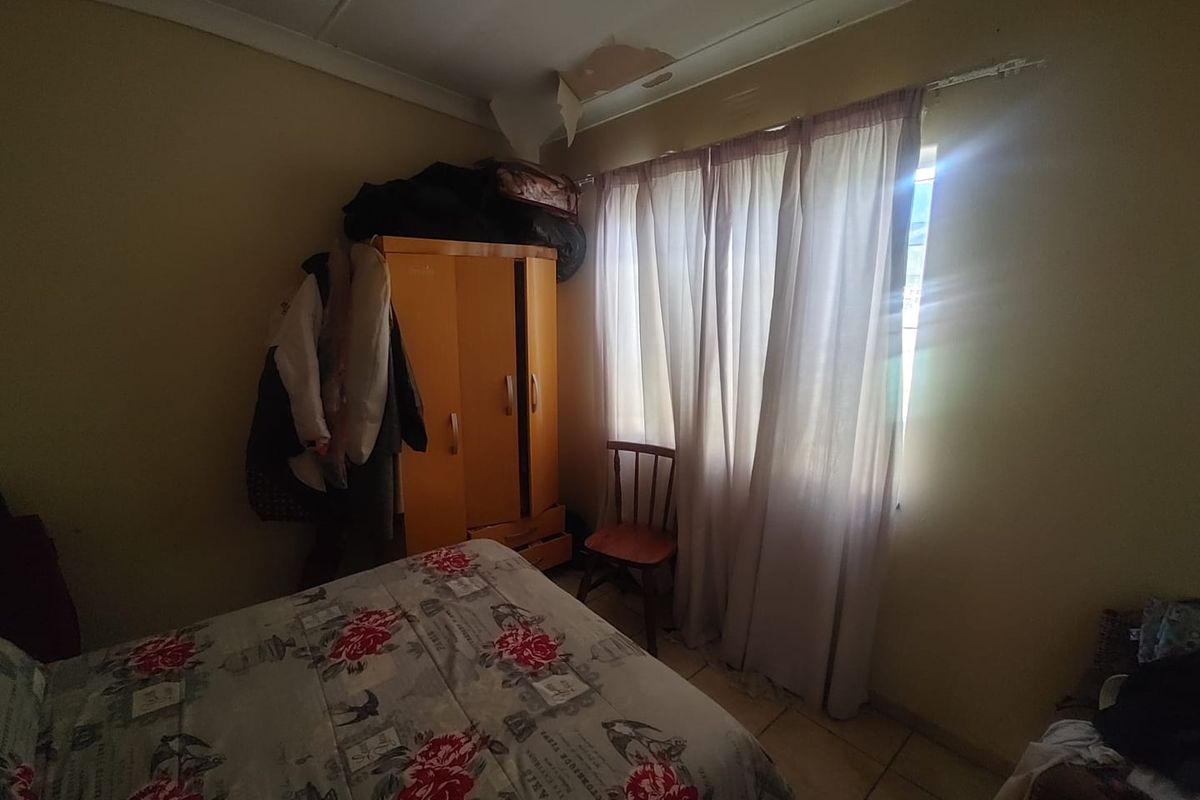 A bedroom featuring tiled flooring and a window with curtains, currently showing signs of ceiling damage requiring repair.