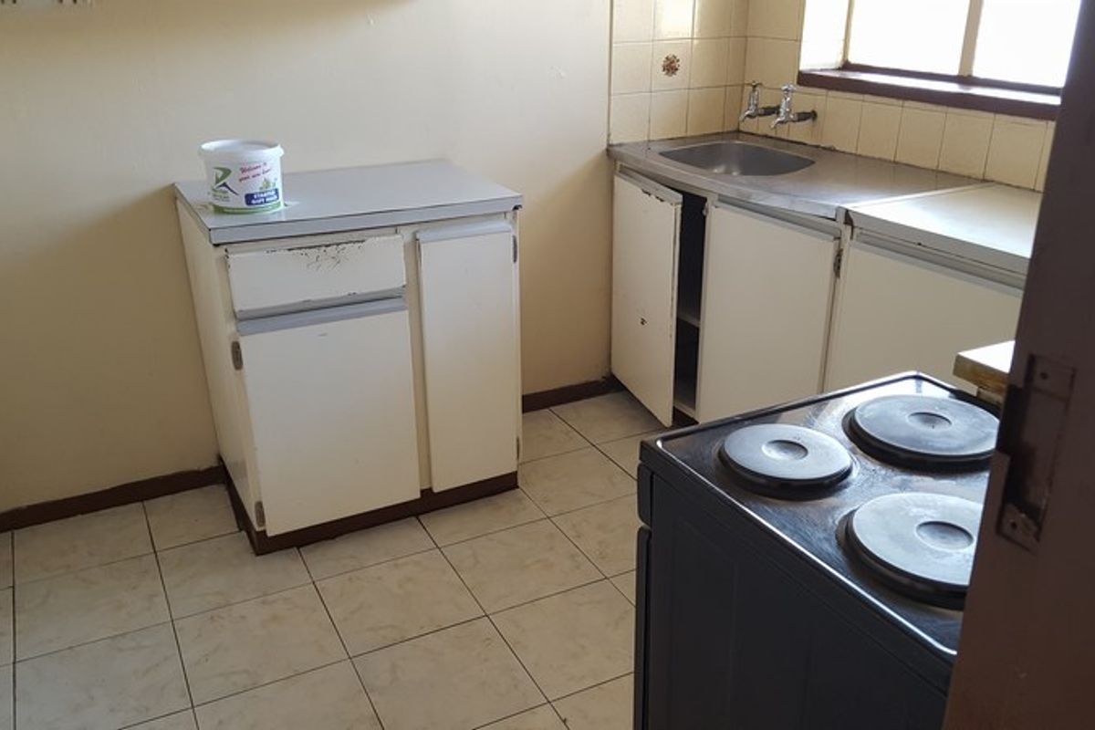 A dated kitchen featuring basic built-in cabinetry, a stainless steel sink, and tiled flooring, offering potential for a modern renovation.
