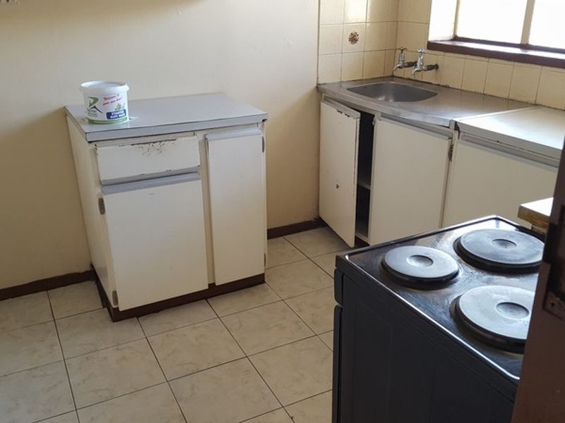 A dated kitchen featuring basic built-in cabinetry, a stainless steel sink, and tiled flooring, offering potential for a modern renovation.