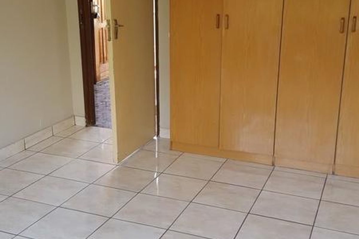 A clean, empty bedroom featuring neutral tiled flooring and functional built-in wooden cupboards, offering a blank canvas for personalization.