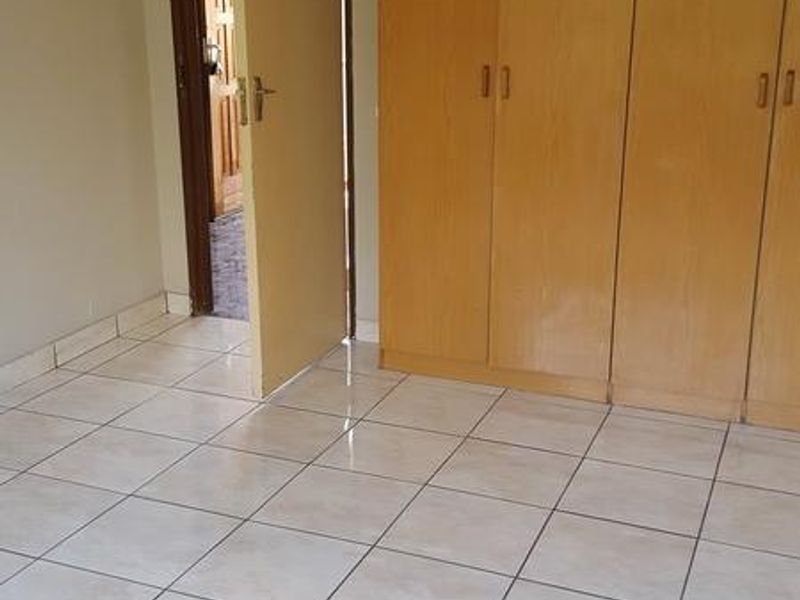 A clean, empty bedroom featuring neutral tiled flooring and functional built-in wooden cupboards, offering a blank canvas for personalization.