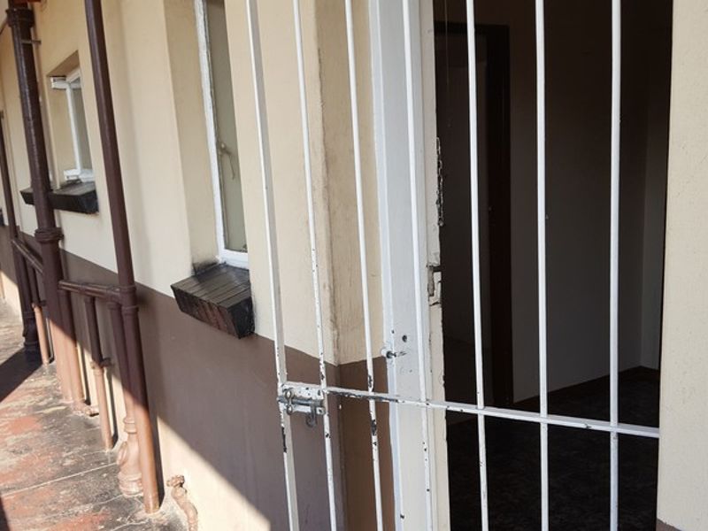 An exterior walkway providing access to the flat, featuring a security gate and showing signs of wear on the floor and wall finishes.
