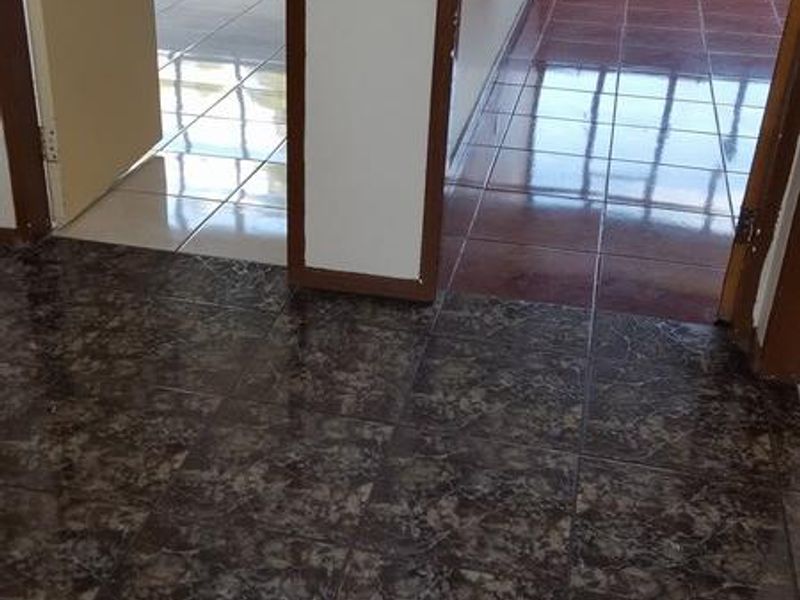 An empty hallway area featuring inconsistent tiled flooring and multiple internal doorways leading to adjacent rooms with large windows.