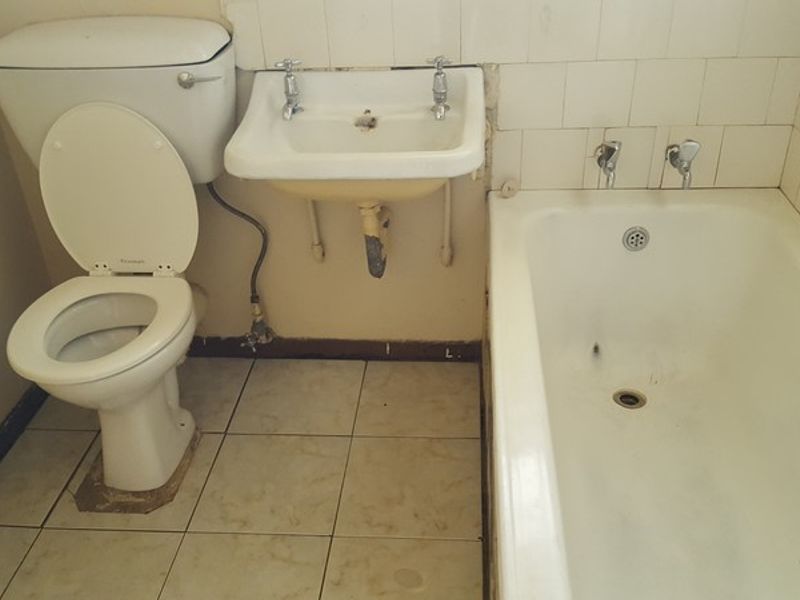 A dated bathroom featuring a standard toilet, wall-mounted basin, and bathtub with ceramic tiling, requiring significant renovation and modernization.