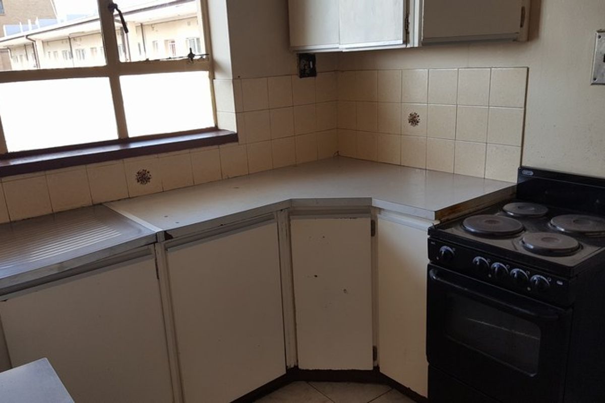 A dated kitchen featuring original cabinetry, laminate countertops, tiled splashbacks, and a freestanding electric stove, offering potential for modernization.
