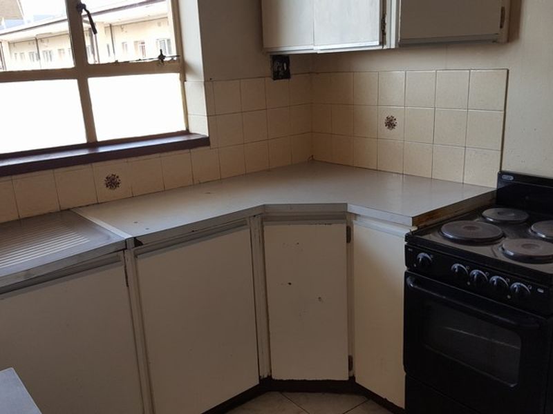 A dated kitchen featuring original cabinetry, laminate countertops, tiled splashbacks, and a freestanding electric stove, offering potential for modernization.