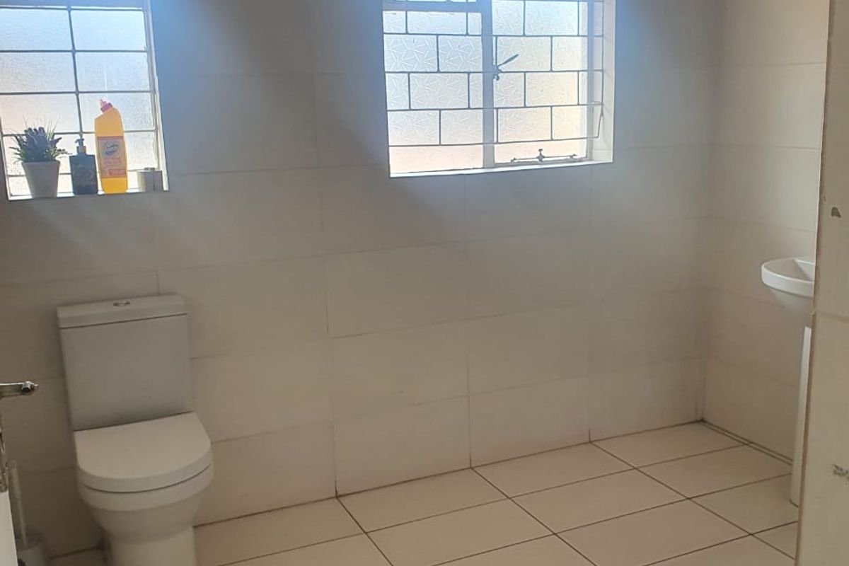 A functional bathroom featuring tiled walls and flooring, a standard toilet, and a pedestal basin with natural light from two windows.