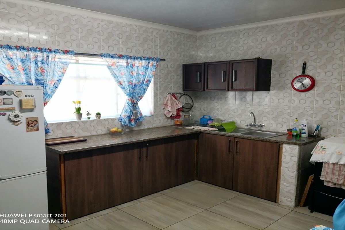 A functional kitchen featuring dark wood-finish cabinetry, laminate countertops, a stainless steel sink, and patterned wall tiles.