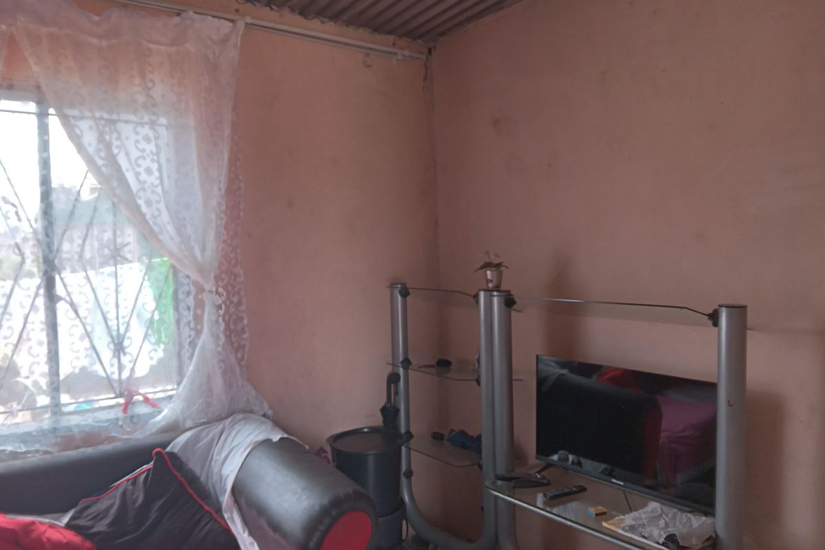 A basic living area featuring a window with security bars and exposed corrugated metal roofing.