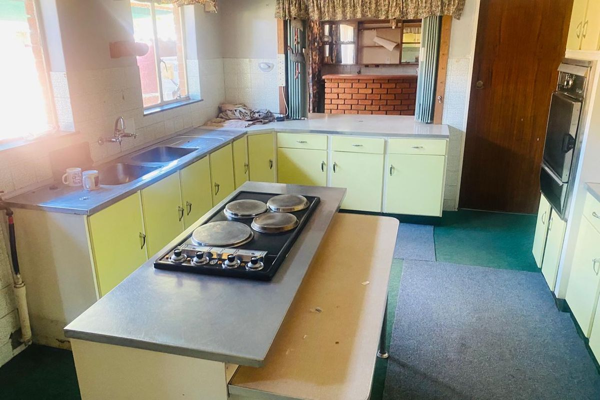 A dated kitchen featuring original cabinetry, a central island with a built-in electric hob, and a wall-mounted oven, offering significant renovation potential.