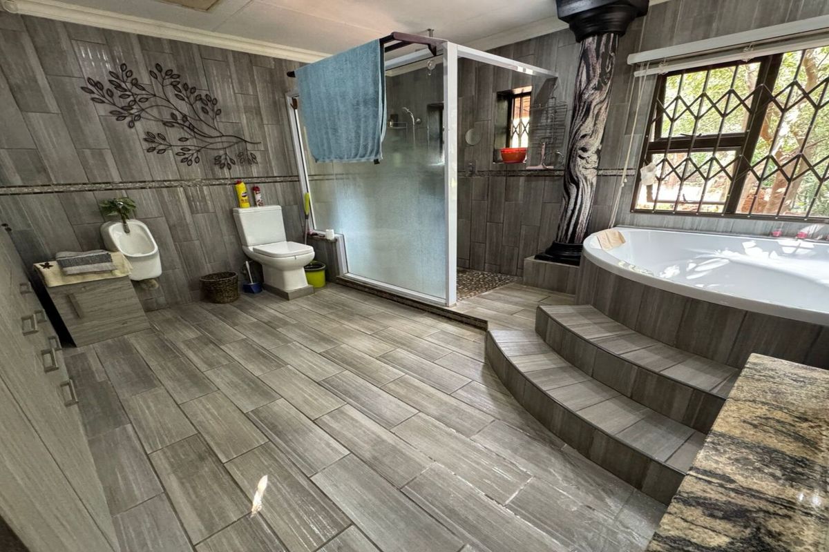 Spacious bathroom featuring a raised corner soaking tub, glass-enclosed shower, wall-mounted urinal, and modern grey wood-look floor and wall tiling.