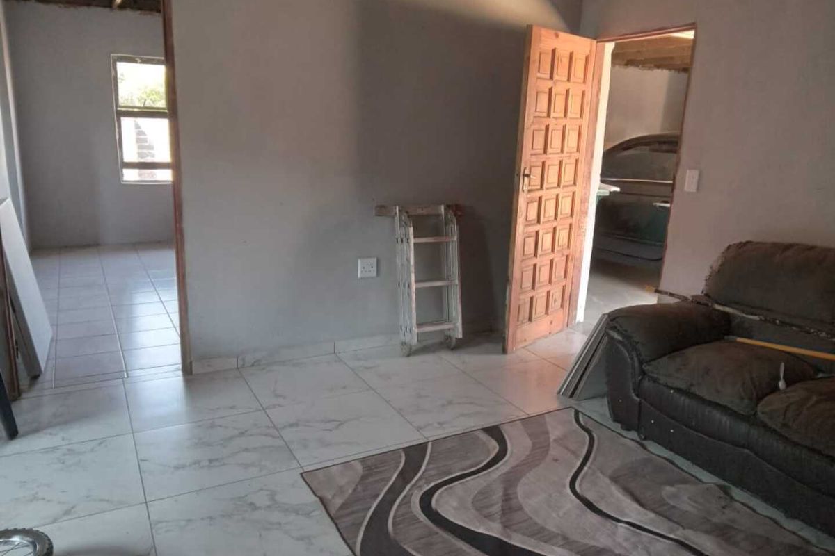 Interior view of a living area featuring tiled flooring and doorways leading to adjacent rooms, with unfinished ceiling details visible.