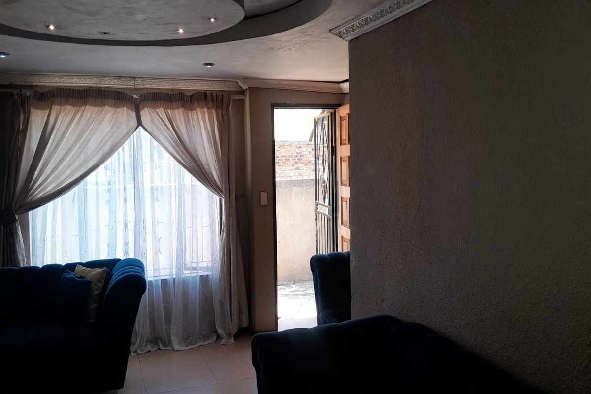 A living room featuring a recessed ceiling with integrated downlights, tiled flooring, and direct access to an outdoor area through a security door.