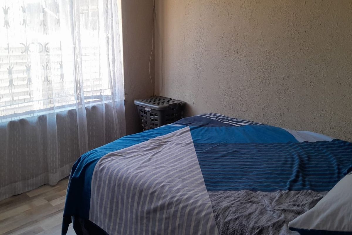 A functional bedroom featuring laminate flooring and a window with sheer curtains, providing natural light.
