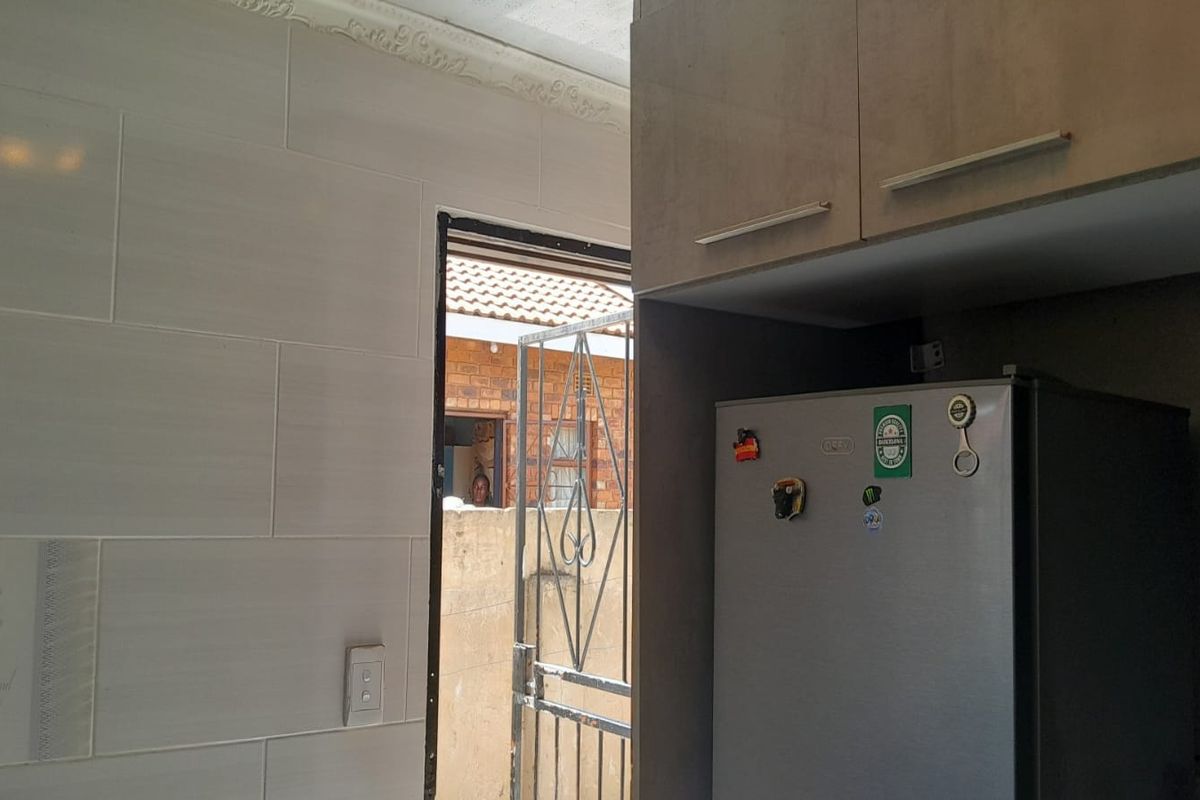 A kitchen area featuring tiled walls, built-in cabinetry, and a doorway leading to an exterior space with a security gate.