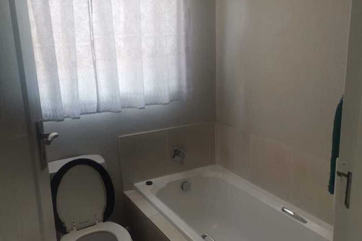 A functional bathroom featuring a built-in bathtub with tiled surround and a standard toilet.