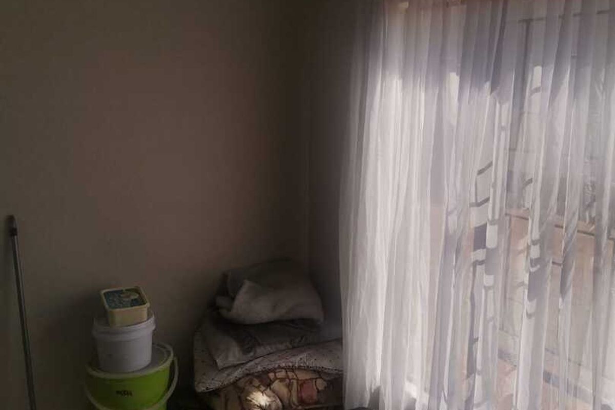 A small bedroom featuring tiled flooring and a large window with sheer curtains, providing natural light to the space.