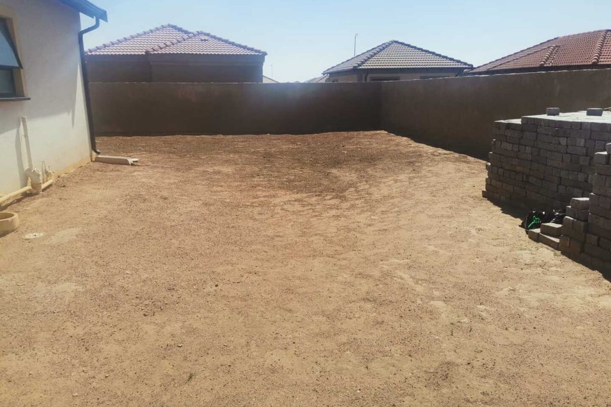 A rear exterior view of the property featuring a large, unlandscaped backyard area enclosed by perimeter boundary walls.