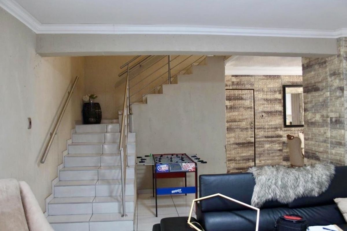 Interior view featuring a tiled staircase with stainless steel handrails, leading to an upper level, adjacent to a living area with textured brick-style wall cladding.