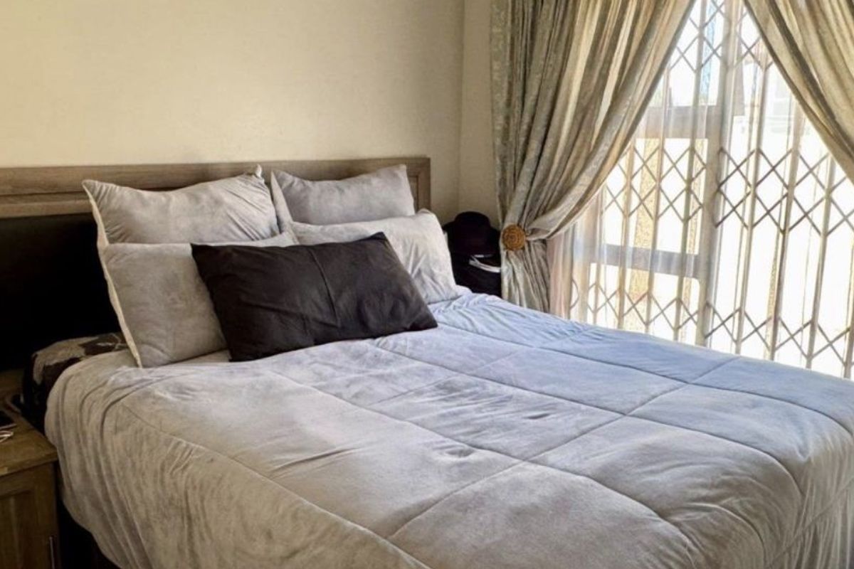 A bedroom featuring a large window with a security gate and neutral wall finishes.