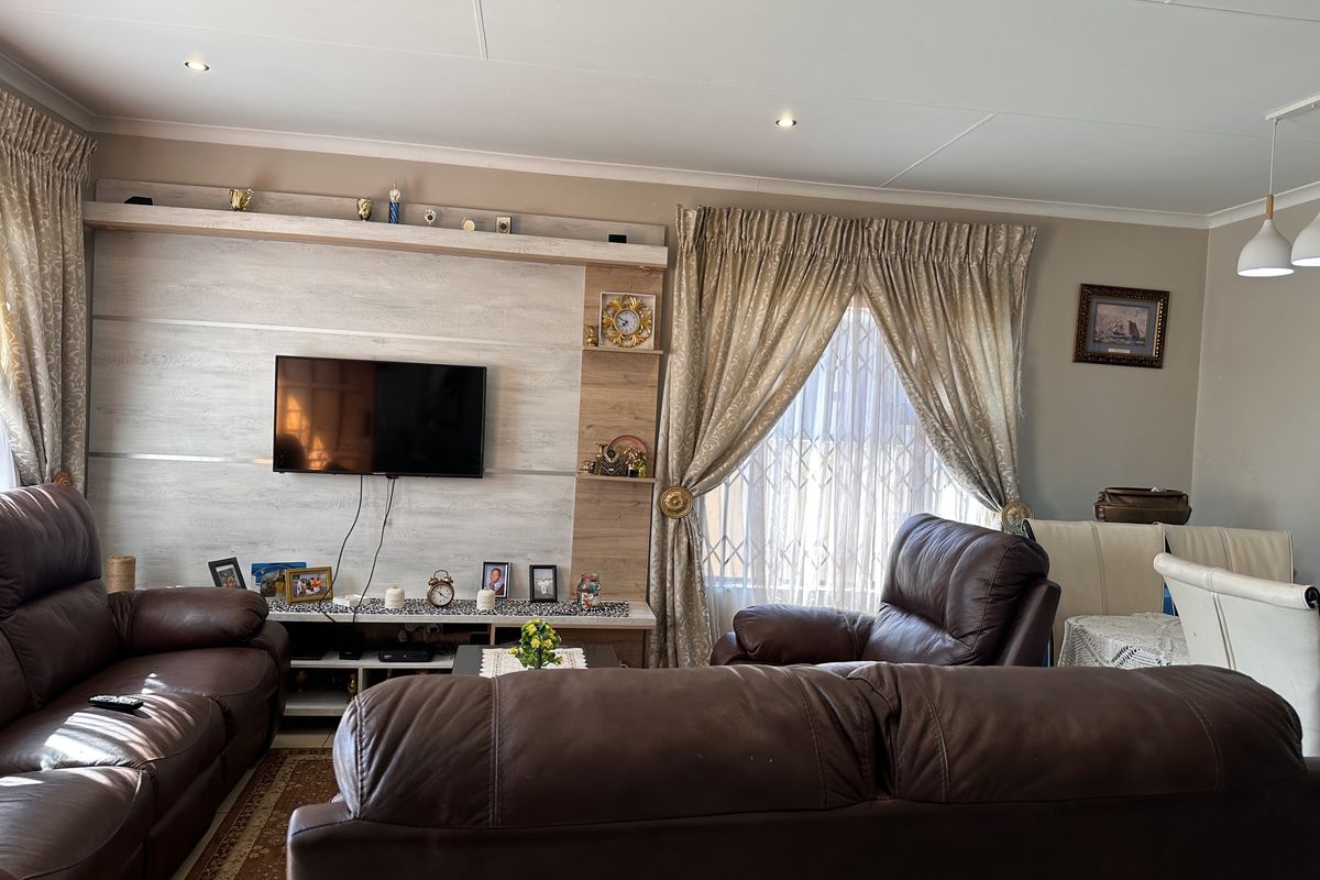 A comfortable living room featuring a built-in media wall unit, recessed ceiling downlights, and large windows with curtain treatments.