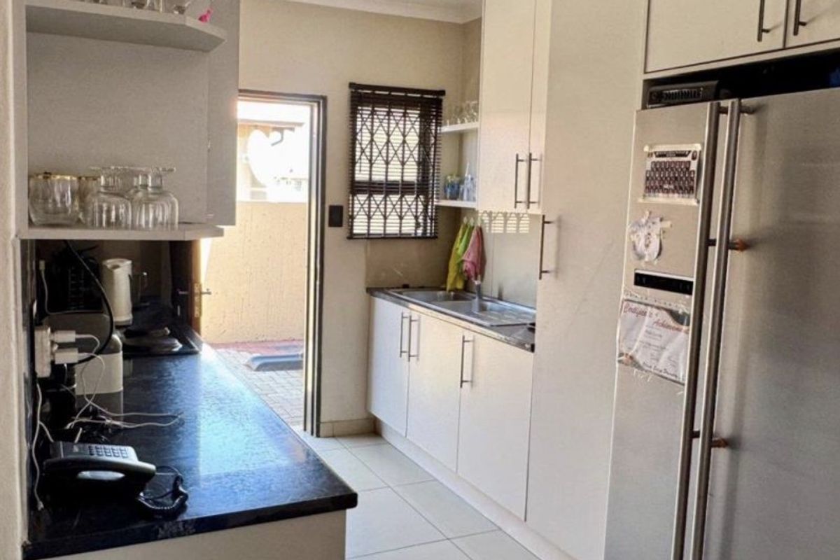 A functional kitchen featuring white cabinetry, dark countertops, a stainless steel sink, and direct access to an outdoor area.