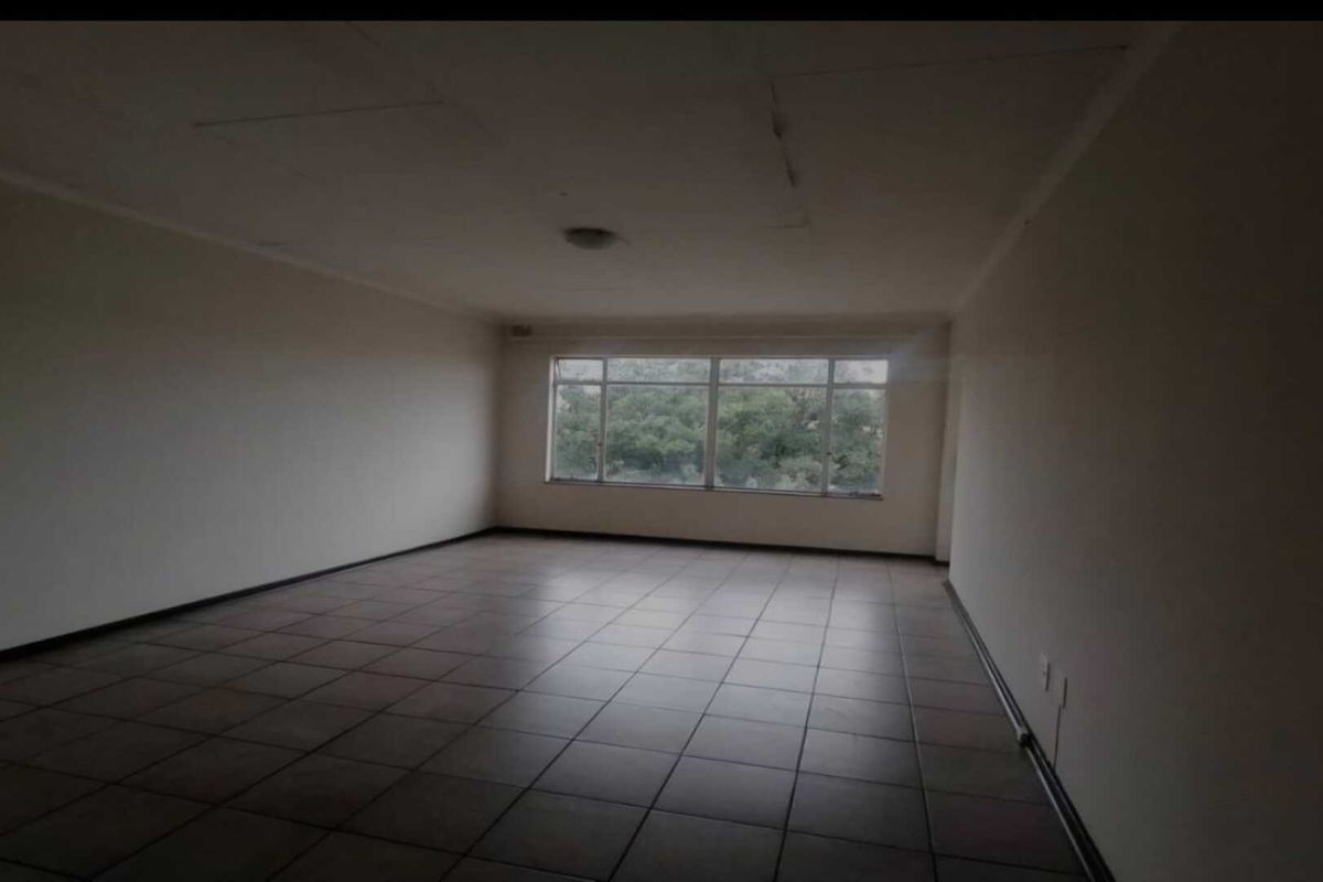 An empty, spacious living area featuring tiled flooring, large windows providing natural light, and a neutral interior finish.