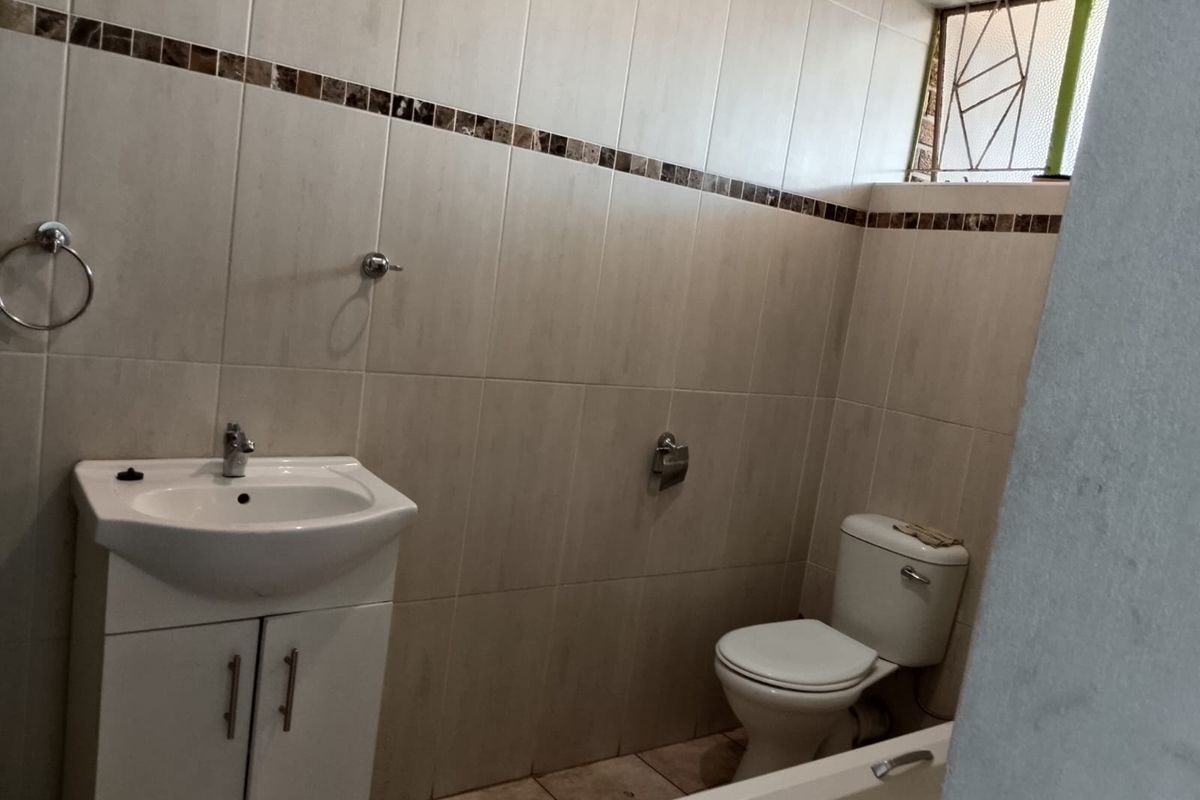 A functional bathroom featuring a vanity basin, toilet, and tiled walls with a decorative border, complemented by a window with security bars.