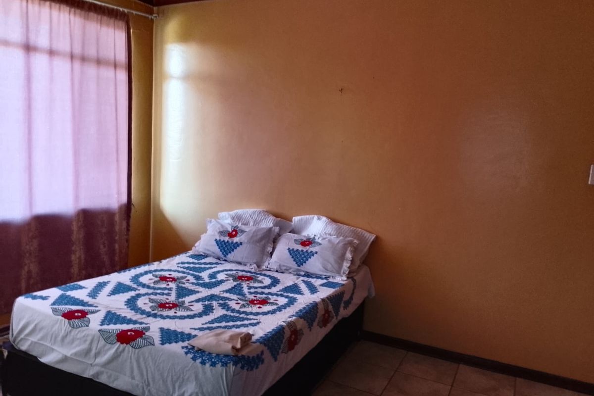 A bedroom featuring tiled flooring and a large window with curtains, providing a functional space with potential for cosmetic updates.