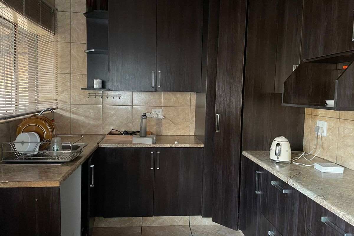 A functional kitchen featuring dark wood cabinetry, stone-look laminate countertops, and tiled splashbacks with integrated storage solutions.