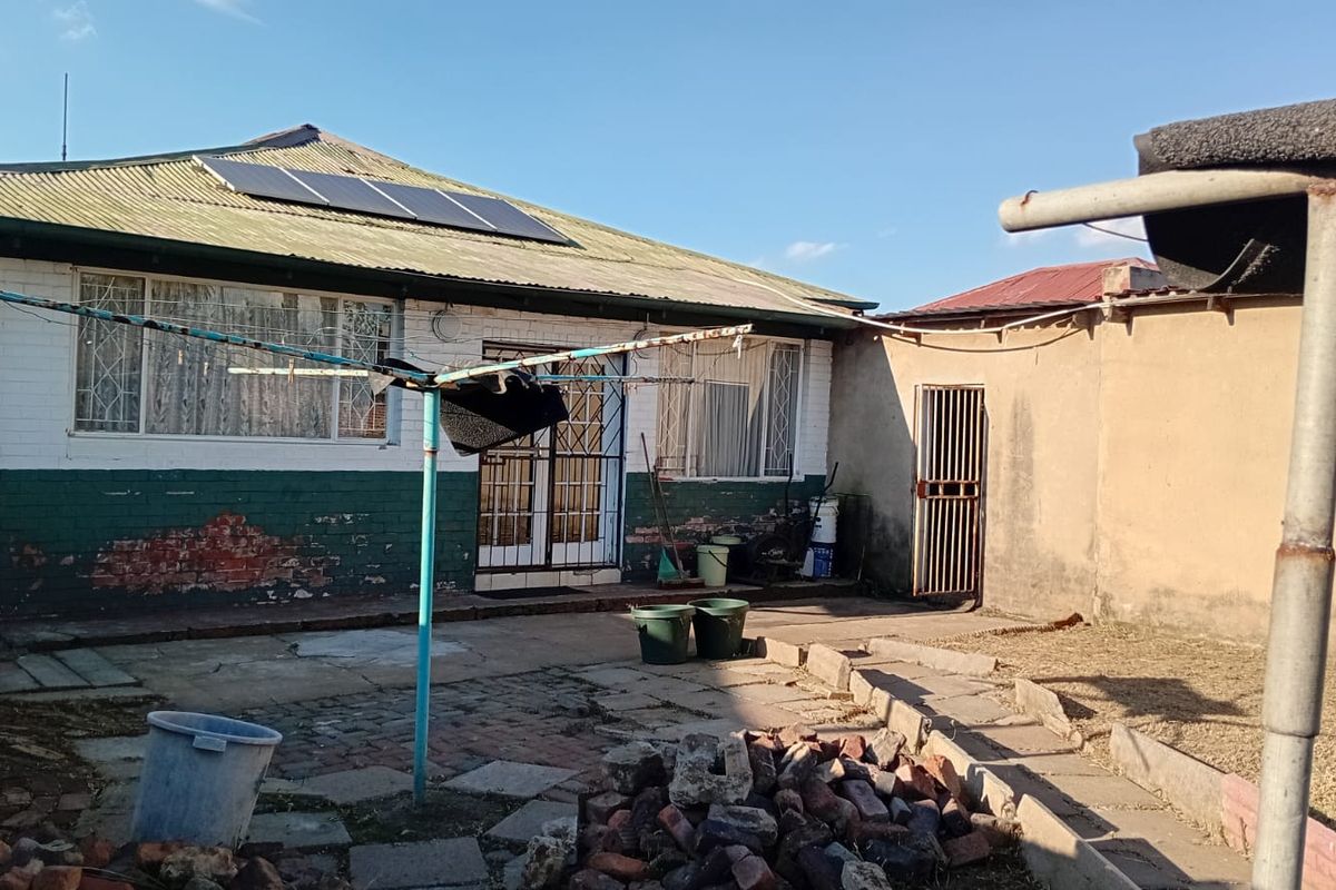 Rear view of the property featuring a paved courtyard, solar panels on the roof, and security gates on the doors and windows.