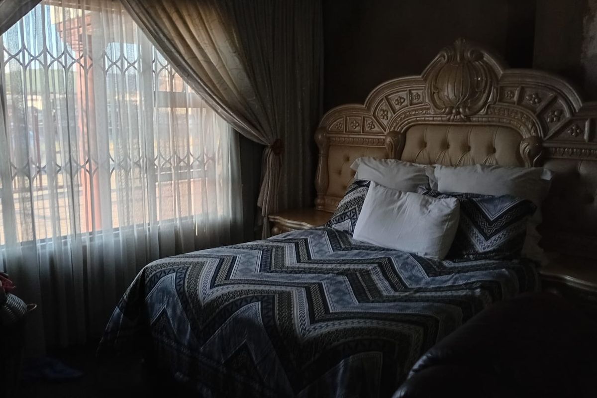 A bedroom featuring a large window with security bars and curtains, providing natural light to the space.