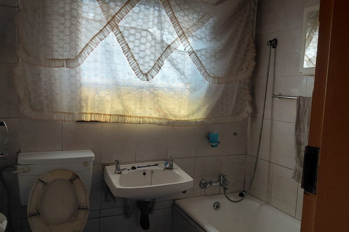 A dated bathroom featuring a standard bathtub with shower attachment, wall-mounted basin, and toilet, finished with full-height wall tiling.