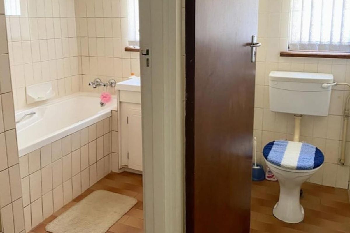 A dated bathroom featuring a built-in bathtub, vanity cabinet, and separate toilet area with original wall tiles and fixtures.