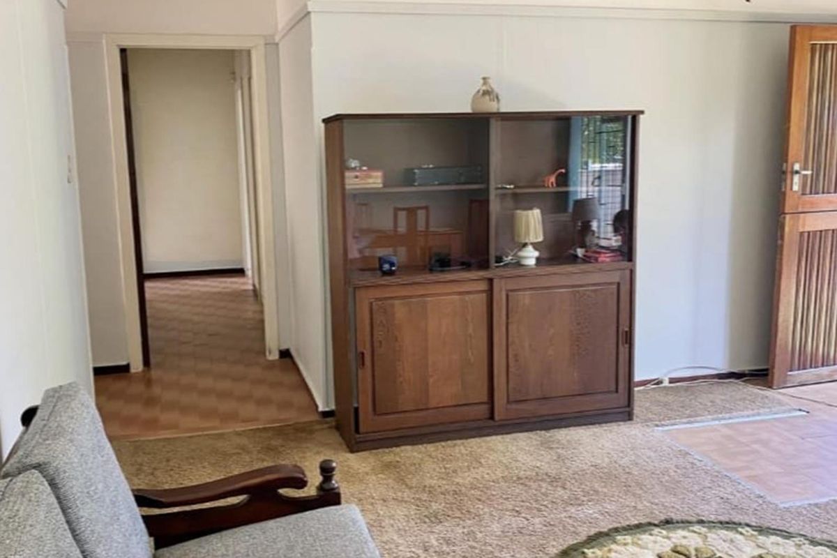 A living area featuring a wooden door and access to a hallway, showcasing dated finishes and carpeting throughout the space.