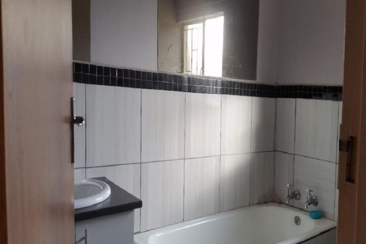 A functional bathroom featuring a built-in bathtub, vanity cabinet with integrated basin, and tiled walls with a decorative black border.
