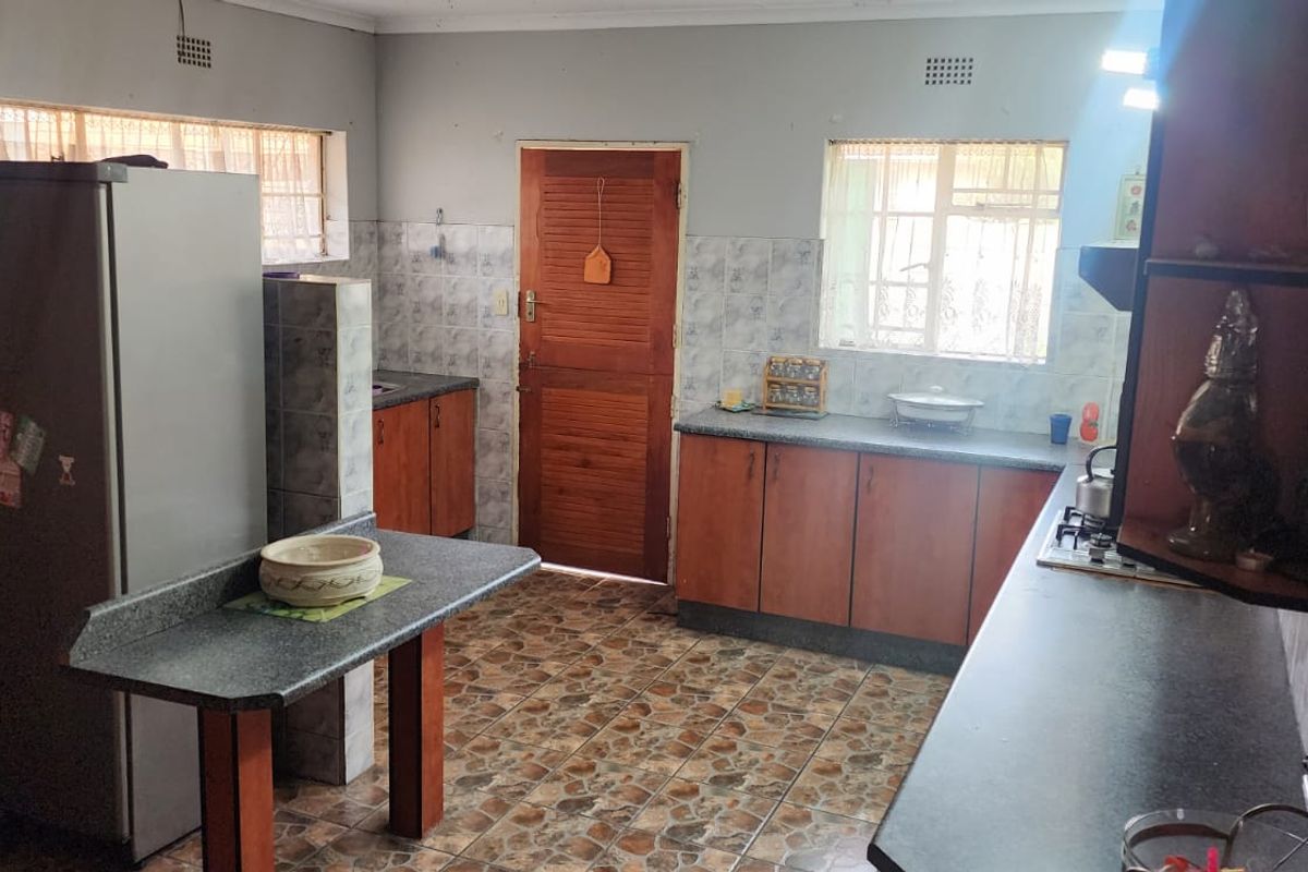 A functional kitchen featuring wooden cabinetry, laminate countertops, tiled splashbacks, and a breakfast bar area with direct exterior access.