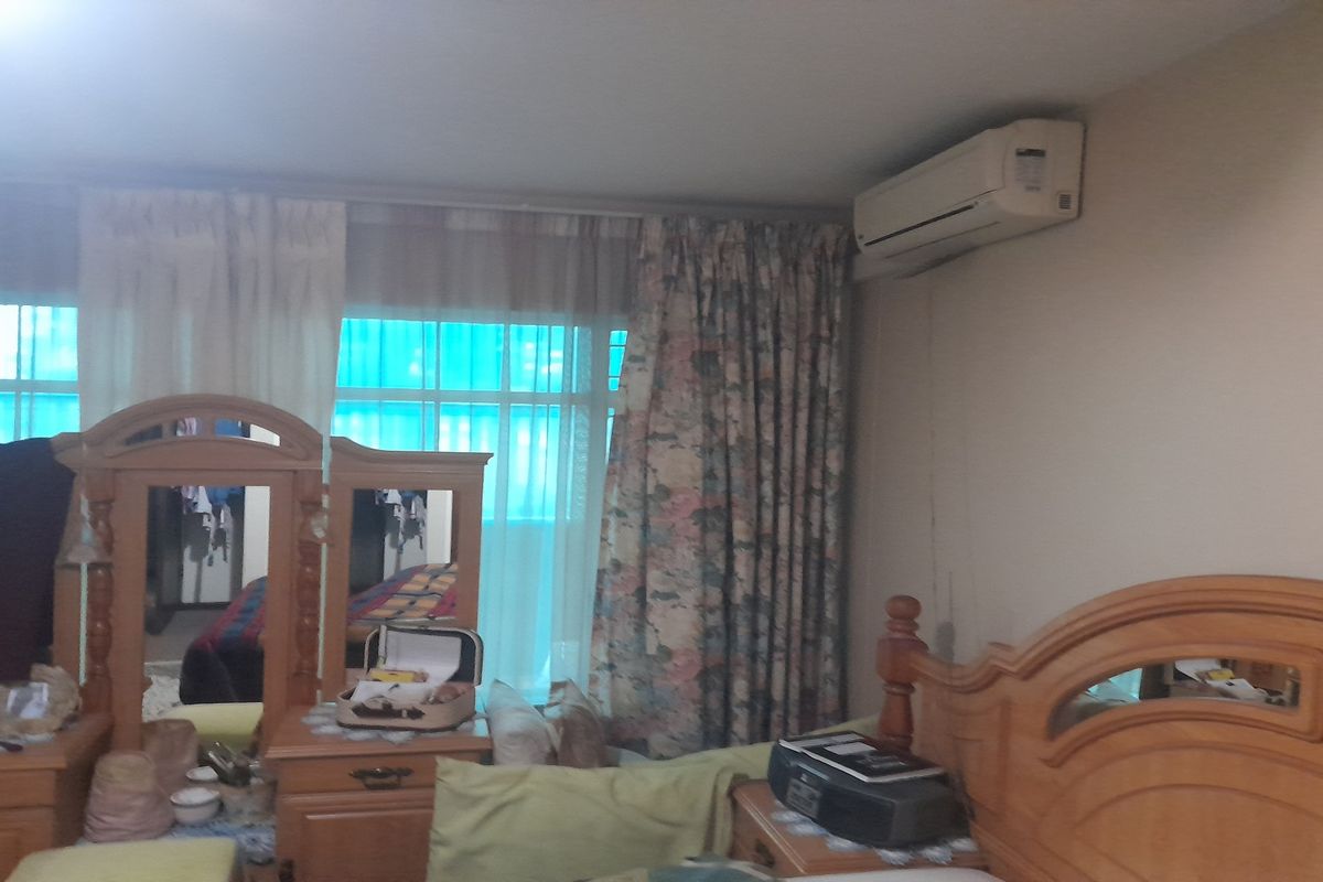 A bedroom featuring a wall-mounted air conditioning unit and large windows with curtains, providing natural light and climate control.