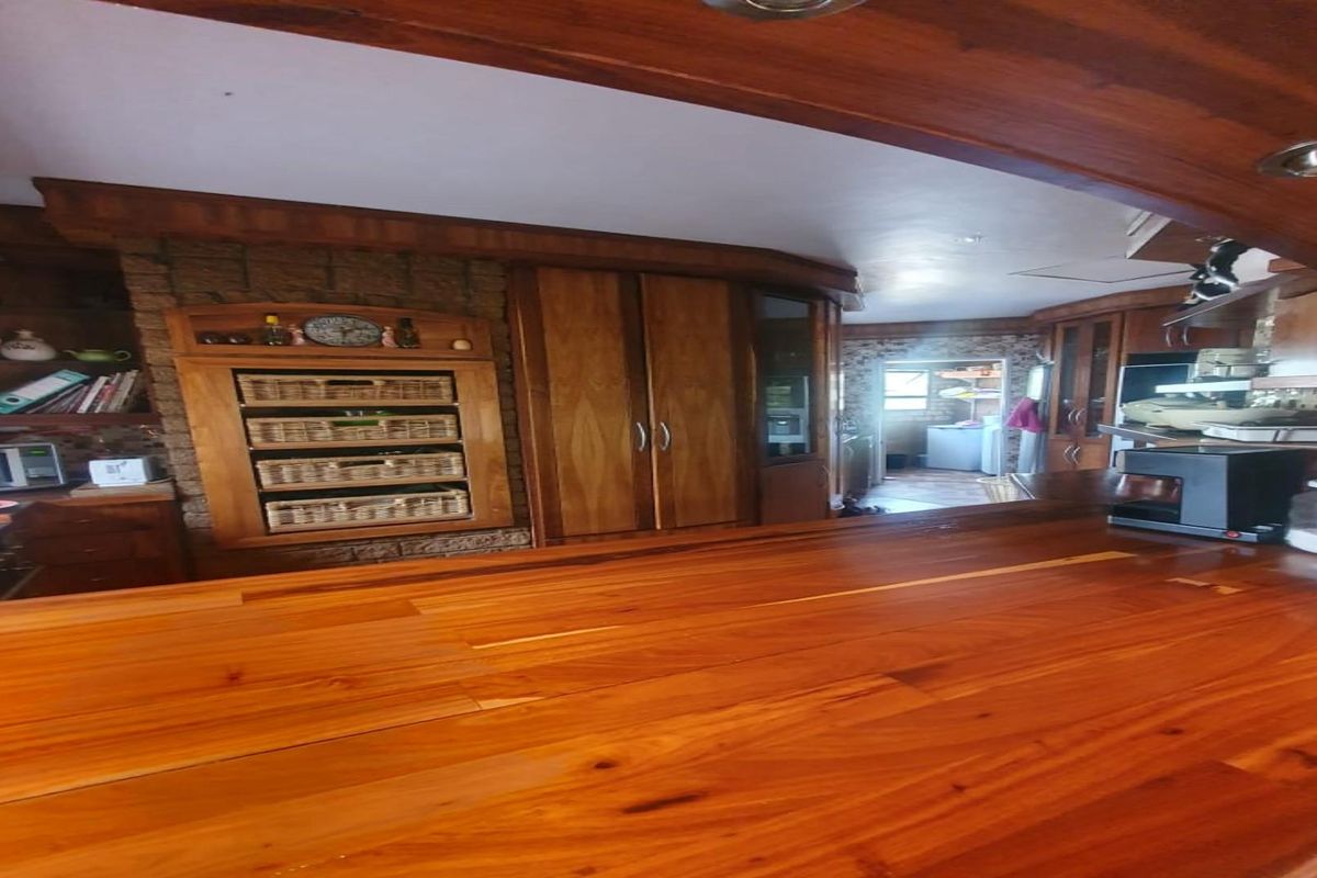 A kitchen featuring extensive timber cabinetry, a large wooden breakfast bar, and a stone-accented wall, with a view through to a secondary utility area.