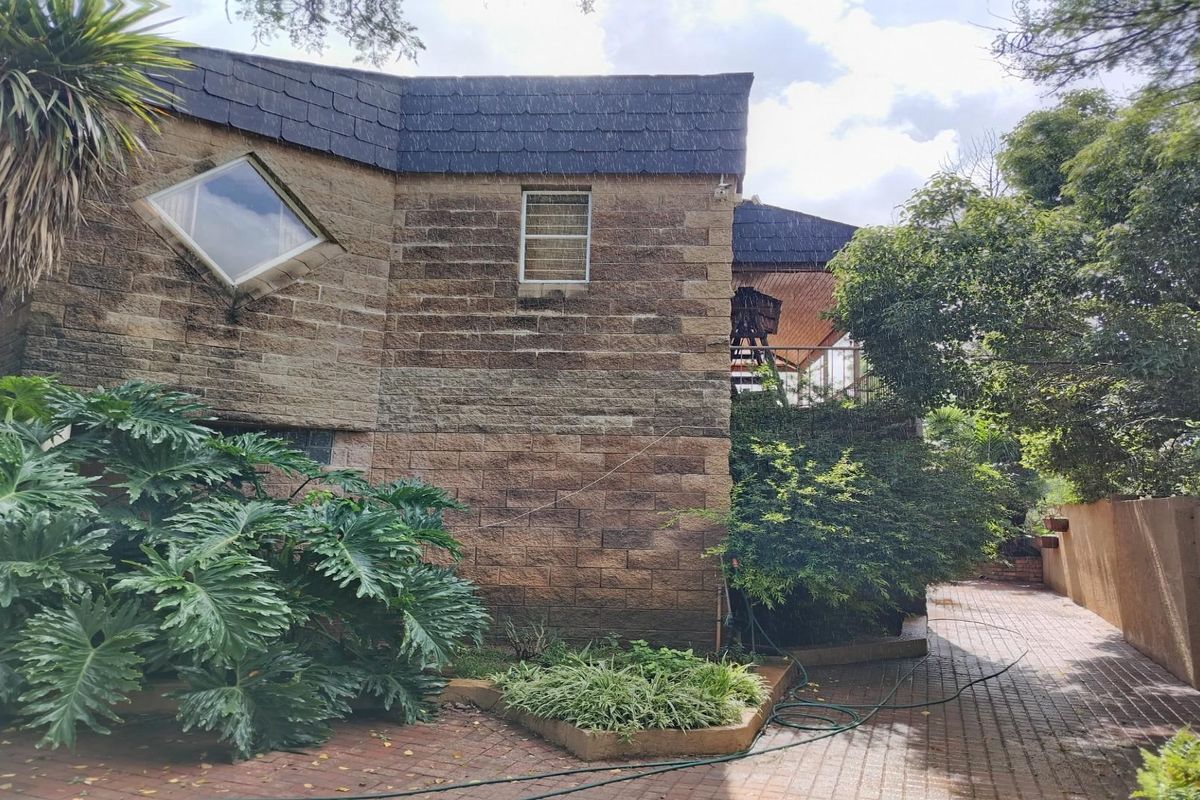 A side view of a stone-clad house featuring a unique diamond-shaped window, tiled roof, and paved walkway surrounded by established garden greenery.