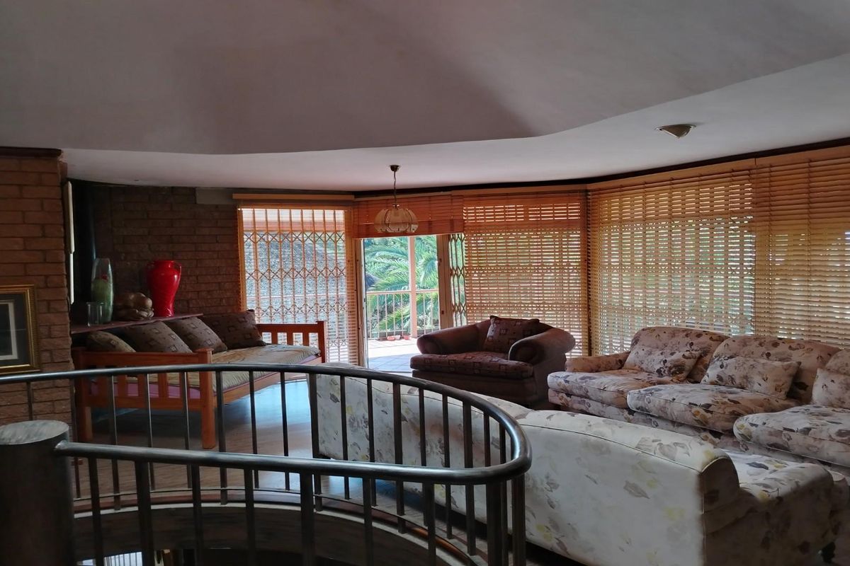 Spacious living area featuring exposed brick walls, a vaulted ceiling, and a curved staircase, with large windows providing natural light and garden access.