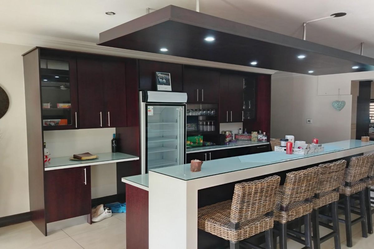 A modern kitchen featuring dark wood cabinetry, a glass-topped breakfast bar, and integrated lighting within a suspended bulkhead ceiling.