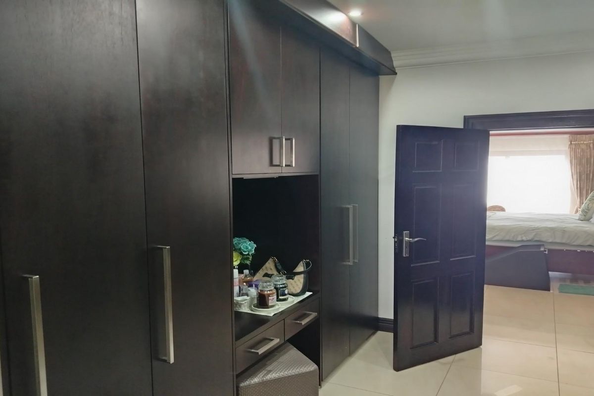 A bedroom featuring extensive dark wood built-in cabinetry with integrated vanity space and tiled flooring, leading into an adjacent bedroom area.