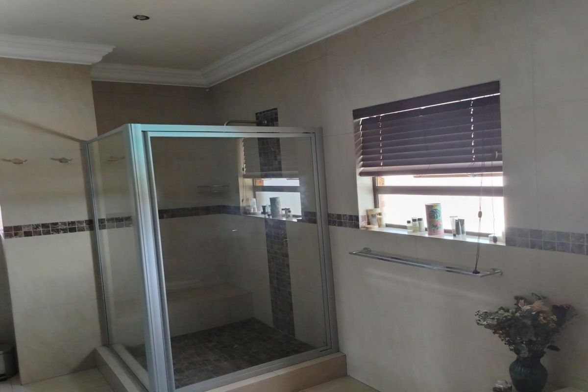 A functional bathroom featuring a glass-enclosed shower, tiled walls with decorative accents, and a window with fitted blinds.