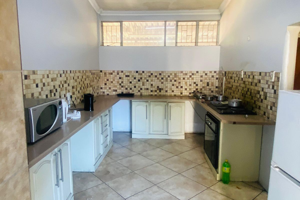 A functional kitchen featuring built-in cabinetry, a tiled backsplash, integrated oven and hob, and tiled flooring with high-level clerestory windows.
