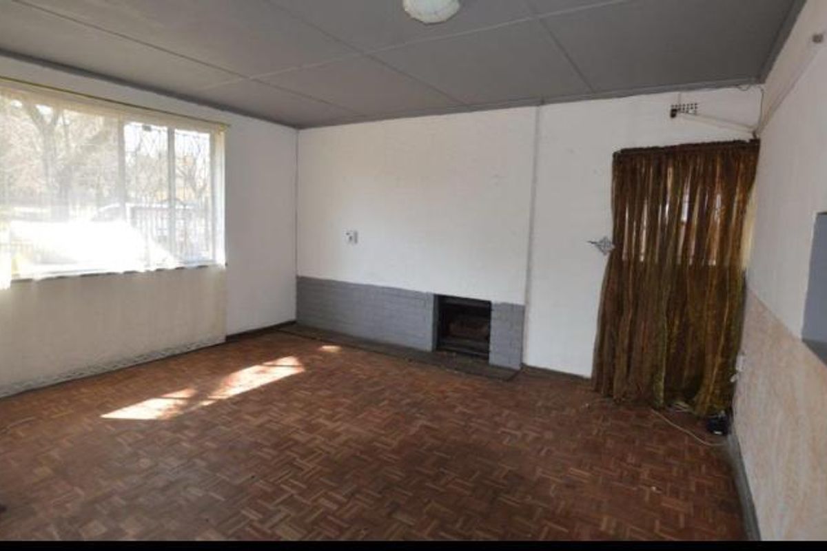 A spacious living room featuring original parquet flooring, a built-in fireplace, and large windows providing natural light.