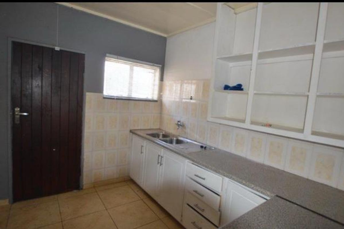 A functional kitchen area featuring built-in cabinetry, a double sink, tiled splashbacks, and direct access via a solid timber door.